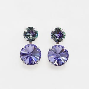 May include: A pair of elegant earrings featuring two round, faceted crystals in shades of purple and teal. The earrings have a silver-colored setting and a post-back closure. The crystals are arranged in a drop style, with a smaller crystal on top and a larger one below.
