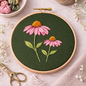 May include: An embroidery hoop featuring two pink coneflowers with orange centers and green leaves, stitched on a dark green fabric. The wooden hoop is held by a brass clasp. The scene is set on a light pink surface with floral accents.