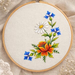 Puede incluir: Diseño floral bordado en un aro de madera. El diseño presenta una gran flor naranja y amarilla, una margarita blanca y acianos azules con hojas verdes. La tela es de color beige claro.