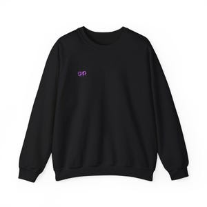 May include: Black crew neck sweatshirt with long sleeves. The sweatshirt features the letters "CHD" in a purple, stylized font on the upper left chest area. The garment is made of a soft material.