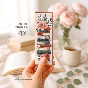 May include: A rectangular cross-stitch bookmark pattern featuring a stack of books adorned with pink flowers and green leaves. The design is presented as a digital download PDF. The bookmark has a white background with a thin brown border.