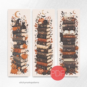 May include: Three vertical cross-stitch patterns featuring stacks of books decorated with autumn leaves, pumpkins, and crescent moons. The designs incorporate dark brown, orange, and cream colors. A red circular PDF icon is visible in the lower right.