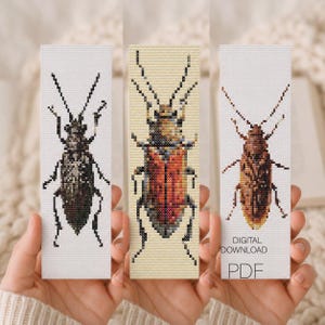 Puede incluir: Tres marcapáginas de punto de cruz con diseños de insectos. Los marcapáginas muestran escarabajos en tonos marrones, negros y rojos. Un marcapáginas tiene el texto "DESCARGA DIGITAL PDF".
