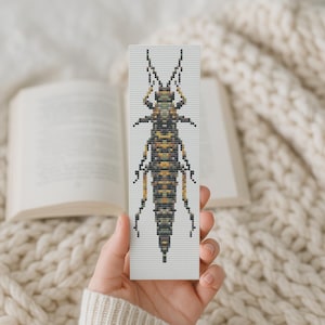 May include: A handmade bookmark featuring a cross-stitch design of an insect. The insect is depicted in shades of brown, yellow, and black, with detailed antennae and body segments. The bookmark is rectangular and set against a soft, neutral background.