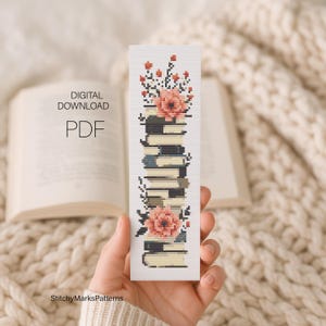 May include: A cross-stitch pattern bookmark featuring a vertical stack of books adorned with peach-colored flowers and dark foliage. The design is printed on white fabric. The text DIGITAL DOWNLOAD PDF is visible on the left side of the image.