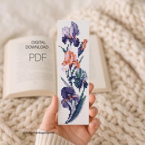 May include: A rectangular cross-stitch bookmark pattern featuring a vertical arrangement of purple, lavender, and peach-colored iris flowers. The design includes the text DIGITAL DOWNLOAD PDF. The pattern is displayed on a white grid background.