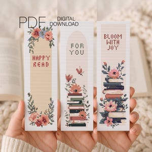 May include: Three cross-stitch bookmarks with floral designs and text. The first bookmark reads "HAPPY READ" with flowers. The second says "FOR YOU" with a stack of books and flowers. The third says "BLOOM WITH JOY" with a stack of books and flowers. "PDF DIGITAL DOWNLOAD" is at the top.