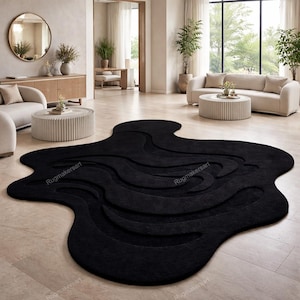 May include: A large, black, abstract-shaped rug with a textured, wave-like design. The rug is the focal point of a modern living room, with neutral-toned furniture and decor in the background. The rug's dimensions are not visible.