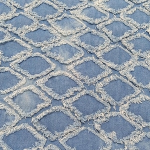 May include: A close-up shot of blue denim fabric featuring a diamond pattern. Each diamond is outlined with a frayed, light-coloured edge, creating a textured effect. The fabric has a faded appearance, with variations in the blue hue.