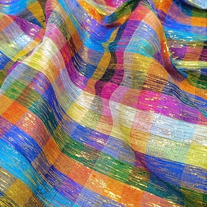Könnte beinhalten: Nahaufnahme eines lebendigen, schimmernden Stoffes mit Karomuster. Der Stoff weist eine Mischung aus Farben auf, darunter Blau, Orange, Lila und Gold. Das Material ist drapiert und erzeugt weiche Falten.