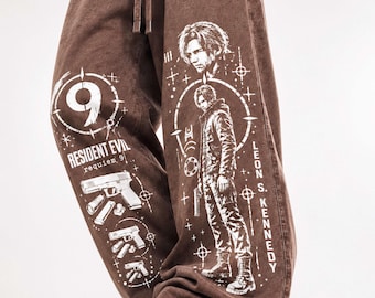 Peut inclure: Pantalon large marron avec des imprimés graphiques blancs représentant Leon S. Kennedy, le texte Resident Evil Requiem 9 et des illustrations de pistolets. Le pantalon possède une taille élastique à cordon et un tissu texturé.