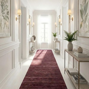 Może przedstawiać: Długi, bordowy dywan w korytarzu z białymi ścianami i listwami. Korytarz posiada kinkiety, oprawione botaniczne nadruki i konsole z elementami dekoracyjnymi. Okno na końcu korytarza zapewnia naturalne światło.