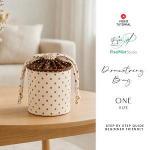 Puede incluir: Una bolsa cilíndrica con cordón que presenta una base de color crema con lunares marrones y un cierre superior de lunares marrones oscuros. La bolsa incluye dos asas de tela y se presenta con texto que indica un tutorial en video y talla única.