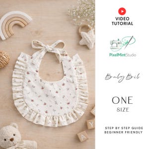 以下が含まれることがあります： 花柄とフリルエッジの白いベビービブ。ビブは結び留めです。木製のおもちゃとブロックがビブを囲んでいます。「Baby Bib」と「ONE SIZE」の文字が見えます。