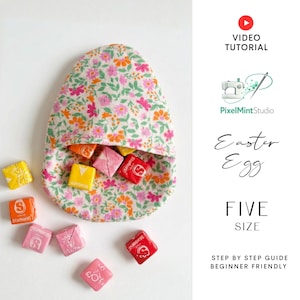 Peut inclure: Une pochette en tissu en forme d'œuf de Pâques remplie de bonbons colorés. La pochette est faite de tissu à motifs floraux dans les tons de rose, d'orange et de vert. Plusieurs bonbons sont éparpillés autour de la pochette. Le texte "Easter Egg" et "FIVE SIZE" est inclus.