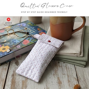 Op de afbeelding: Een wit doorgestikt brillenkoker met kleine rode stippen en een enkele rode drukknoopsluiting. De koker heeft verticale stiklijnen en een kleine metalen clip aan de bovenste flap. De tekst Quilted Glasses Case Step By Step Guide Beginner Friendly is bovenaan zichtbaar.