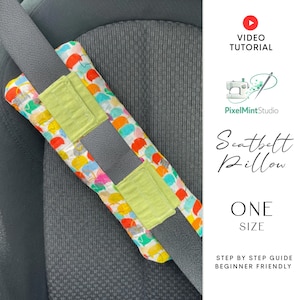 Puede incluir: Una almohada colorida para cintur&oacute;n de seguridad con un estampado de paraguas rojos, amarillos, azules y verdes. La almohada est&aacute; sujeta a un cintur&oacute;n de seguridad gris y tiene un parche verde lima. El texto "Seatbelt Pillow" y "One Size" son visibles.