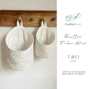 May include: Two quilted fabric pods with a white background and black polka dots hang from a wooden rack. The pods have white interiors and fabric loops for hanging. The image also includes the text "PixelMintStudio", "Quilted Fabric Pod", "TWO SIZE", and "STEP BY STEP GUIDE BEGINNER FRIENDLY".