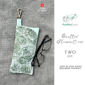 Peut inclure: Un étui à lunettes matelassé avec un motif cachemire vert et blanc, doté d'un fermoir doré. L'étui est ouvert, révélant une paire de lunettes à monture noire. Le texte sur l'image indique "Quilted Glasses Case" et "TWO SIZE".