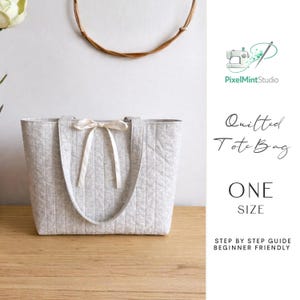 May include: A light gray quilted tote bag with a cream-colored bow. The bag has vertical stitching and two handles. The text on the right side of the image reads "Quilted Tote Bag" and "ONE SIZE".