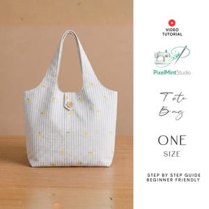Op de afbeelding: Een wit en grijs gestreepte tote bag met gele citroenaccenten en een houten knoopsluiting. De tas heeft een enkel compartiment en twee handvatten. Tekst op de afbeelding luidt "Tote Bag" en "ONE SIZE".