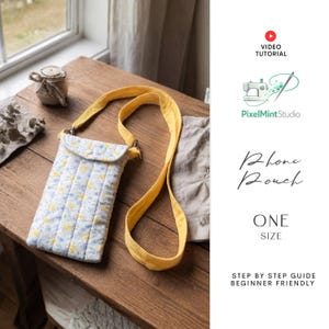 May include: A quilted phone pouch with a yellow strap, featuring a floral pattern in blue and yellow on a white background. The pouch is on a wooden table, with the text "Phone Pouch" and "One Size" visible.