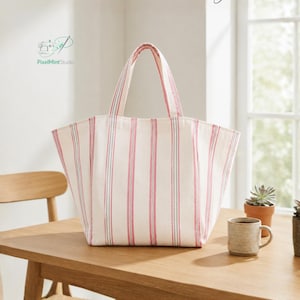 May include: A tote bag featuring a cream-colored fabric with vertical pink and thin grey stripes. The bag has two top handles and a wide, open-top design. Text at the top reads "Curved Tote Bag" and at the bottom "STEP BY STEP GUIDE BEGINNER FRIENDLY".
