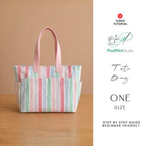 Op de afbeelding: Een pastelkleurige gestreepte draagtas met roze handvatten en accenten. De tas heeft verticale strepen in roze, blauw en groen. De tekst "Tote Bag" en "ONE SIZE" zijn zichtbaar.
