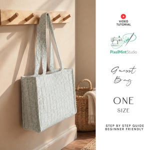 May include: A light gray quilted tote bag with vertical stitching and two shoulder straps hanging from a wooden wall hook. The image includes text reading Video Tutorial, PixelMintStudio, Guest Bag, One Size, and Step by Step Guide Beginner Friendly.