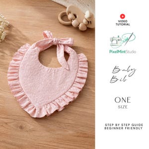 May include: A pink baby bib with a ruffled edge and a bow at the neck. The bib has a polka dot pattern and is made of soft fabric. The text "Baby Bib" and "ONE SIZE" are visible.
