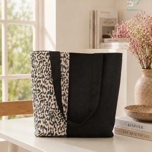 May include: A tote bag featuring a vertical split design with one side in a black and white leopard print and the other side in solid black fabric, including two matching black fabric shoulder straps and the text STEP BY STEP GUIDE BEGINNER FRIENDLY.