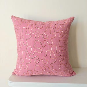 May include: Pink throw pillow with a white and pink embroidered pattern.