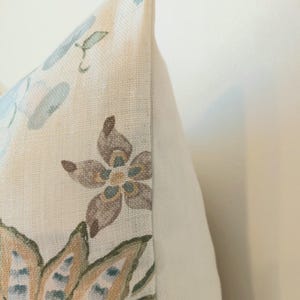 May include: Close-up of a decorative pillow with a floral pattern. The pillow features a cream-colored background with a design of blue, brown, and green flowers and leaves. The pillow has a white side.