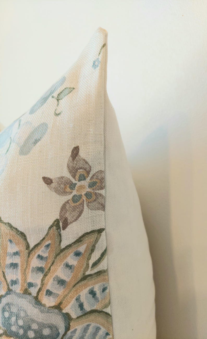 May include: Close-up of a decorative pillow with a floral pattern. The pillow features a cream-colored background with a design of blue, brown, and green flowers and leaves. The pillow has a white side.