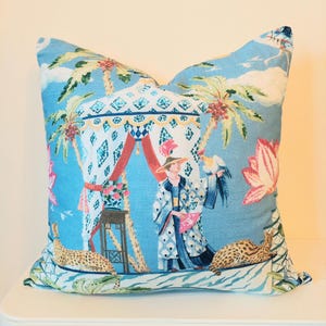 May include: A decorative cushion with a blue backdrop, showcasing a detailed illustration. The design includes palm trees, a figure in elaborate clothing, and two leopard-like creatures. The cushion has a tropical, exotic theme.