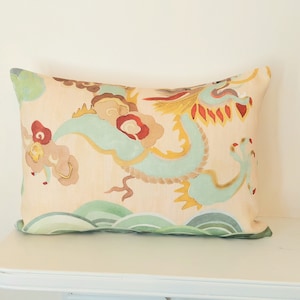 Puede incluir: Una almohada decorativa con un fondo beige que presenta un diseño de dragón verde y dorado. El dragón está rodeado de flores y nubes rojas y amarillas. La almohada es perfecta para agregar un toque de estilo inspirado en Asia a cualquier habitación.