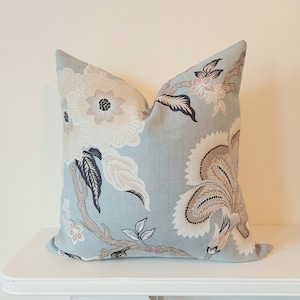 Könnte beinhalten: Ein blaues Kissen mit einem floralen Muster in Braun-, Beige- und Schwarztönen. Das Kissen zeigt eine große Blume in der Mitte und kleinere Blumen und Blätter drumherum.