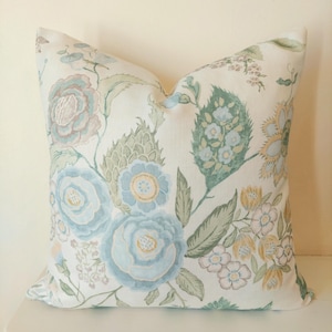 May include: A decorative pillow with a floral pattern. The pillow features large blue and pink flowers with green leaves on a cream background. The design has a vintage, botanical aesthetic, suitable for home decor.
