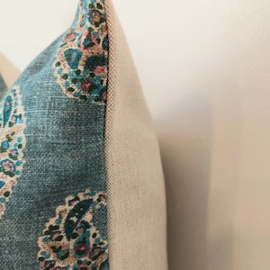 May include: Close-up of a blue and white patterned pillow with a beige backing. The pillow has a paisley design with pink, green, and blue accents.