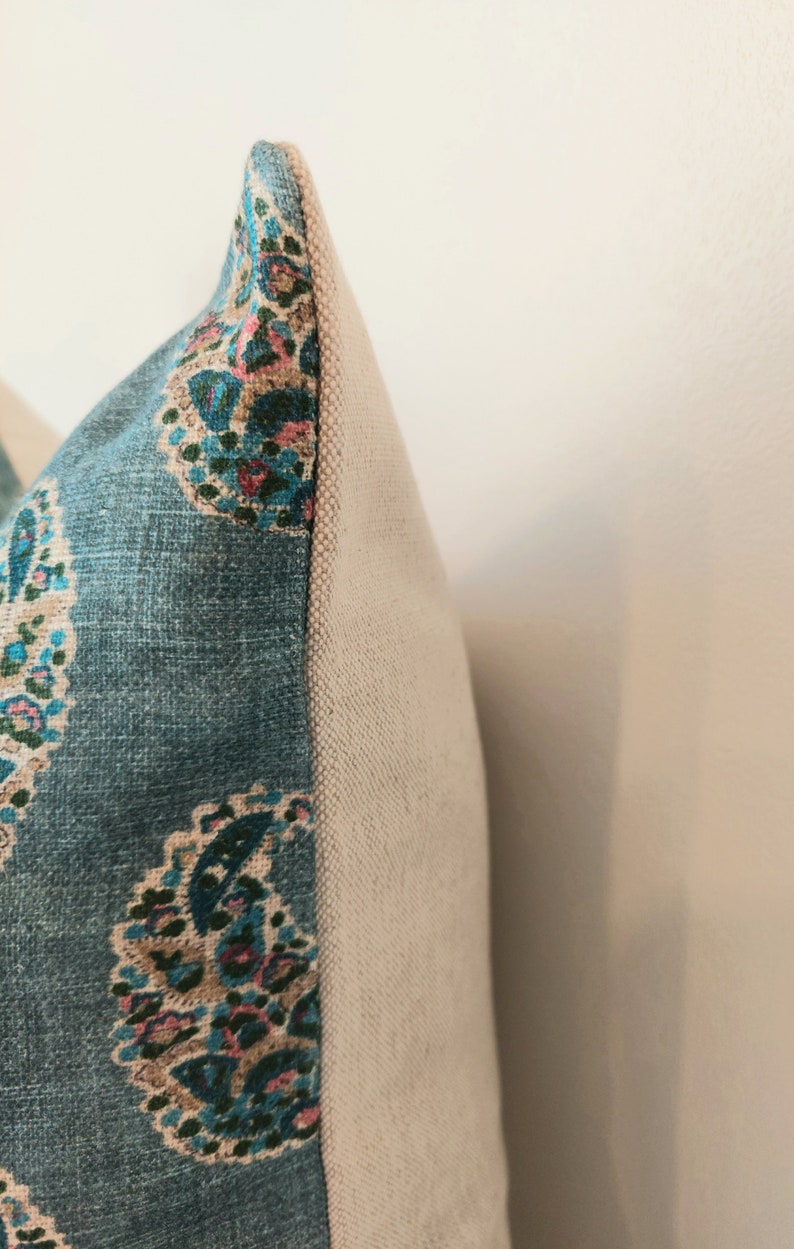 May include: Close-up of a blue and white patterned pillow with a beige backing. The pillow has a paisley design with pink, green, and blue accents.