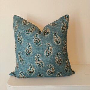 May include: A teal blue throw pillow with a paisley pattern in shades of pink, green, and gold.