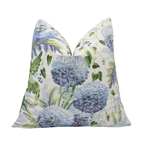 Op de afbeelding: Een vierkant sierkussen met een witte achtergrond en een botanische print van grote, ronde blauwe en paarse alliumbloemen, groene varenbladeren en kleine donkerblauwe bessen. De stof heeft een zachte textuur en een volle, stevige vorm.