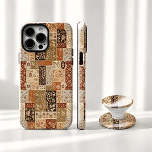 May include: A smartphone case and a matching circular collapsible phone grip featuring a patchwork design of rectangular panels. Each panel displays intricate floral and botanical patterns in a colour palette of burnt orange, cream, and dark brown.