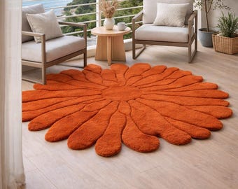 May include: An orange, flower-shaped rug with a textured surface. The rug is placed on a wooden floor on a balcony, with two chairs and a small table. The background shows a view of the ocean and a clear sky.