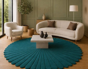 May include: A teal, round rug with a petal-like design dominates the foreground of a living room scene. The rug is centered beneath a square, light-colored coffee table. A cream-colored sofa and armchair, along with decorative vases, complete the room's decor.