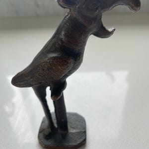 May include: A dark brown, textured metal nutcracker shaped like a parrot perched on a stand. The parrot has a curved beak and is depicted with its mouth open. The entire object is cast in a single piece with a rough, weathered finish.