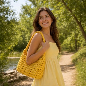 Puede incluir: Un bolso de hombro de ganchillo en color amarillo brillante con un patrón de puntos gruesos y texturizados y una sola correa integrada. El bolso está hecho de hilo y tiene una forma rectangular estructurada con una abertura superior.