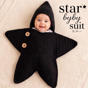 Puede incluir: Un saco para bebé en forma de estrella tejido a ganchillo en color negro, con capucha puntiaguda y dos botones de madera marrón claro en la parte frontal. El texto "star byby suit" aparece en negro arriba a la derecha con iconos de estrellas y corazones.