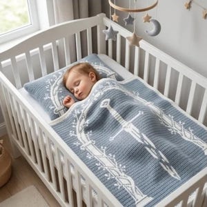 Puede incluir: Un conjunto de manta y almohada de punto para bebé en azul y blanco, con un patrón detallado de espada y arco floral. El conjunto está colocado dentro de una cuna de madera blanca, con un móvil de estrellas y luna suspendido encima.