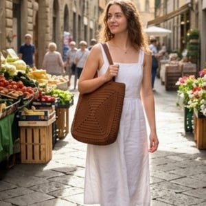 Puede incluir: Un bolso tote de ganchillo marrón con textura de patrón cuadrado y una sola correa para el hombro, llevado junto a un vestido midi blanco sin mangas con escote cuadrado y un corpiño ajustado que fluye hacia una falda relajada.